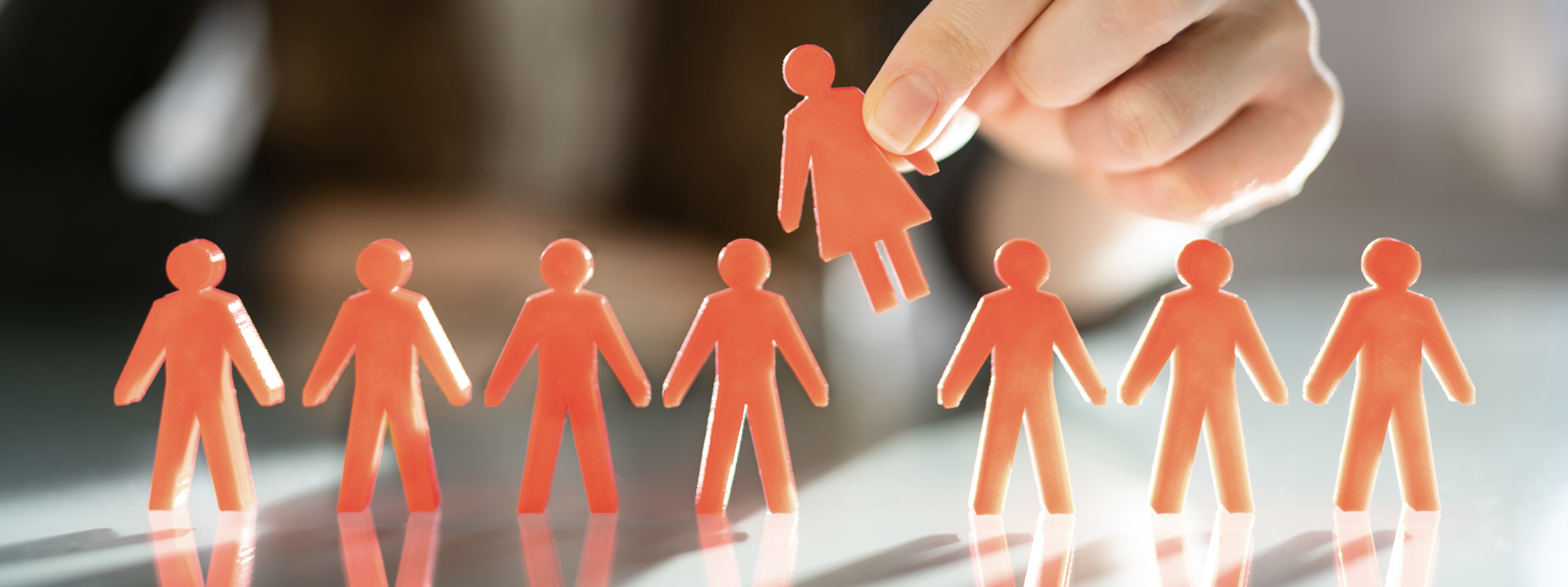 A row of plastic orange figurines, with a hand holding one of the figurines up in the air. 