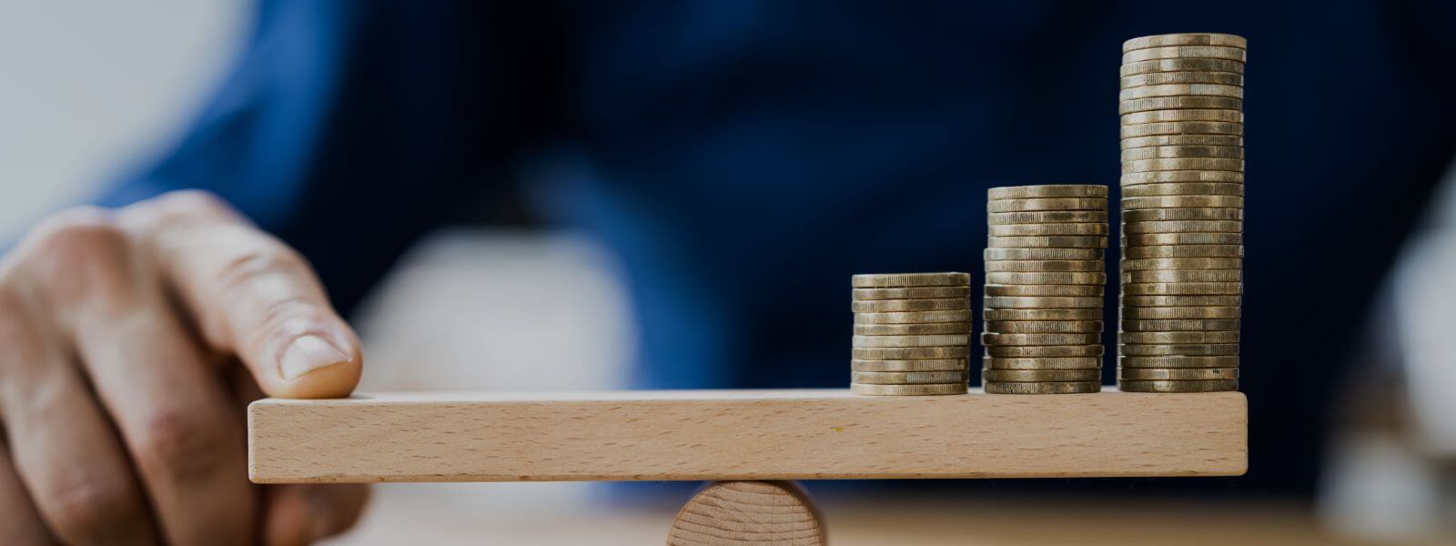 A scale that balances coins on one side and a person's hand holding down the other side. 