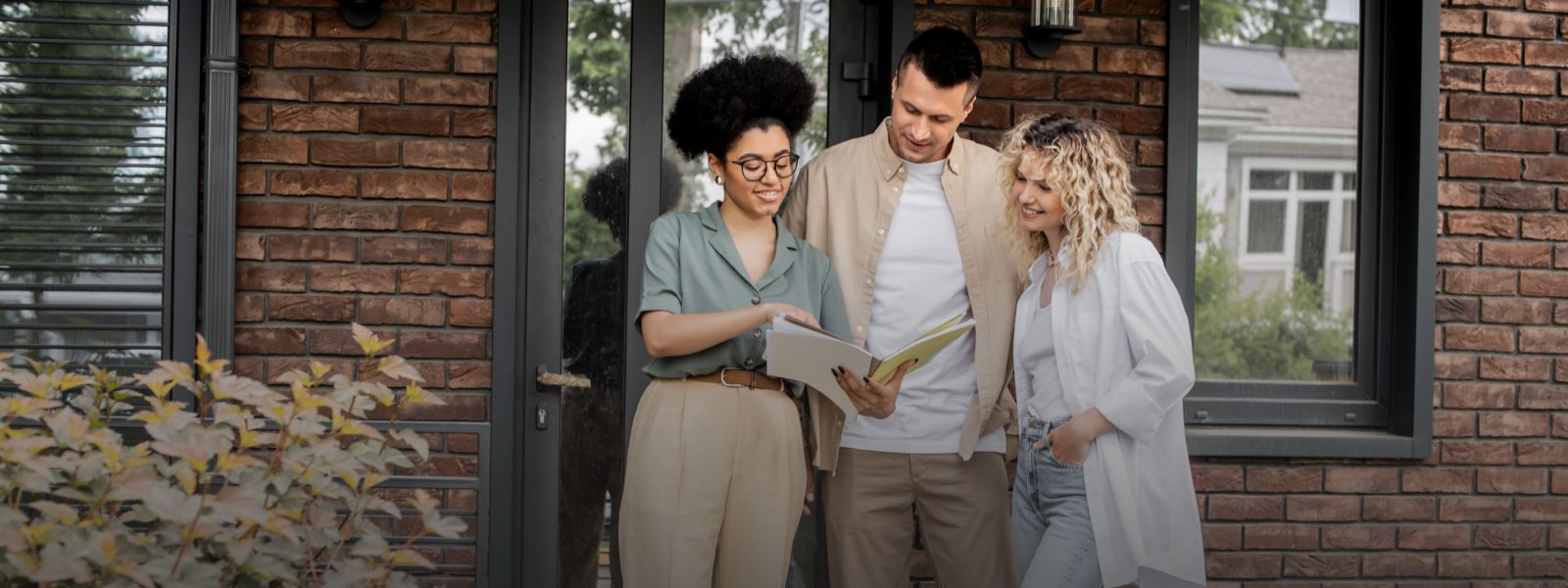 Three people looking at a smartphone in front of a house.