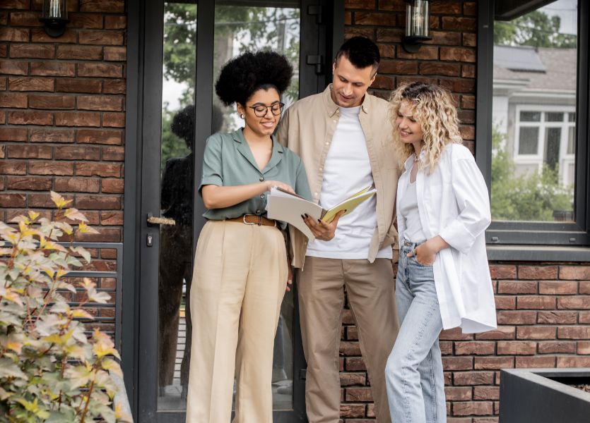 Three people looking at a smartphone in front of a house.