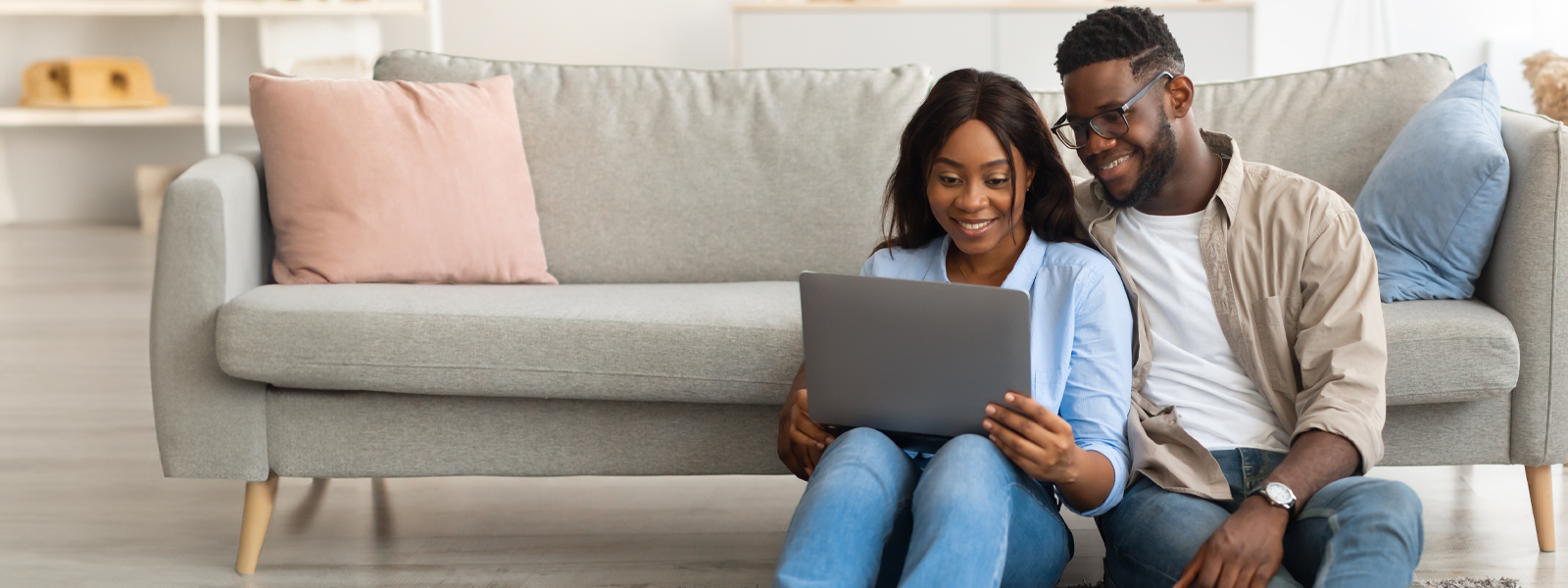 A couple in their living room, browsing a laptop while smiling. 